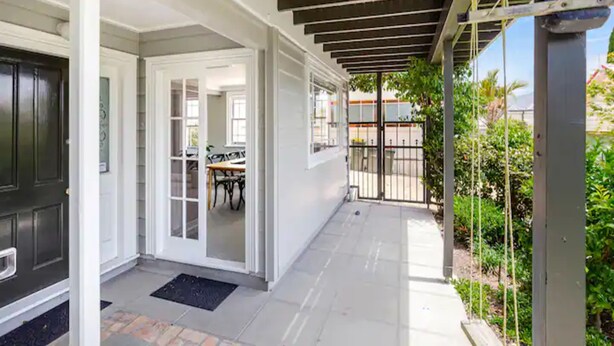 Un patio techado con techo de madera, una puerta negra y vista a un comedor a través de puertas de cristal.