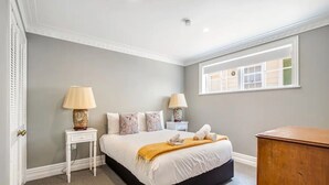 Un dormitorio con una cama, dos mesitas de noche con lámparas, una ventana y un aparador de madera.