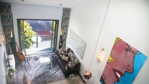 A modern living room with a large window, a sofa, a coffee table, and a painting on the wall. - One-bedroom loft in Viaduct by Zodiak Stays (Auckland)