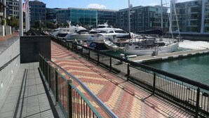 A marina with several yachts docked, a paved walkway with a patterned design, and modern buildings in the background. - One-bedroom loft in Viaduct by Zodiak Stays (Auckland)