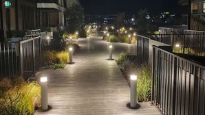 Une promenade nocturne, agrémentée de bornes régulièrement espacées et d’un chemin en bois, bordée d’immeubles dotés de balcons et de garde-corps.