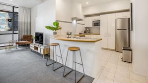 Una cocina moderna con una isla central, electrodomésticos de acero inoxidable y una zona de estar con una silla y taburetes.