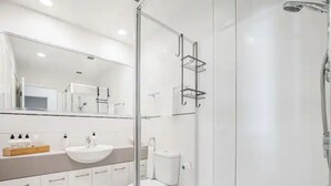 Un baño moderno con cabina de ducha de vidrio, un lavabo blanco y un inodoro.