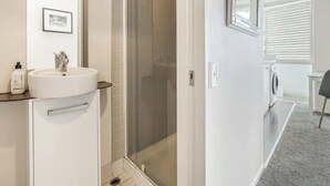 A modern bathroom with a glass-enclosed shower, a sink with a mirror, and a framed picture on the wall. - Tidy Apartment With Balcony (Auckland)