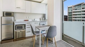 A modern kitchen with white cabinets, stainless steel appliances, and a dining area with a table and two chairs. - Tidy Apartment With Balcony (Auckland)