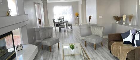 A modern living room with a fireplace, two grey armchairs, a brown sofa, and a glass coffee table.