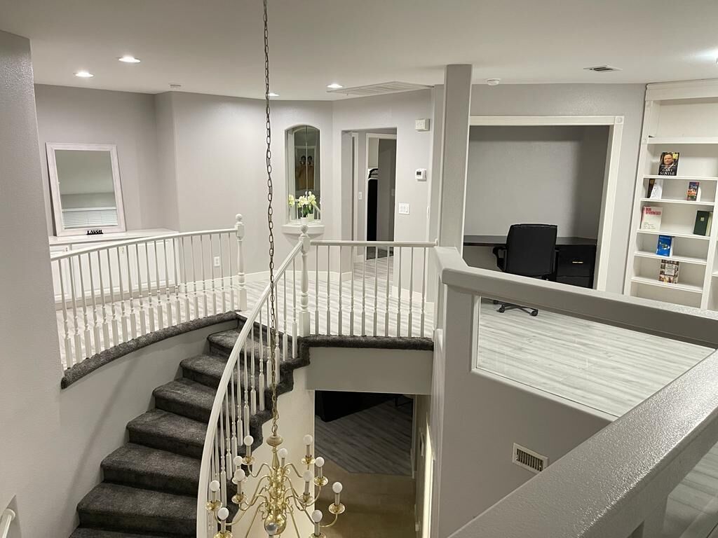 A multi-level home interior with a staircase, a chandelier, and a bookshelf.