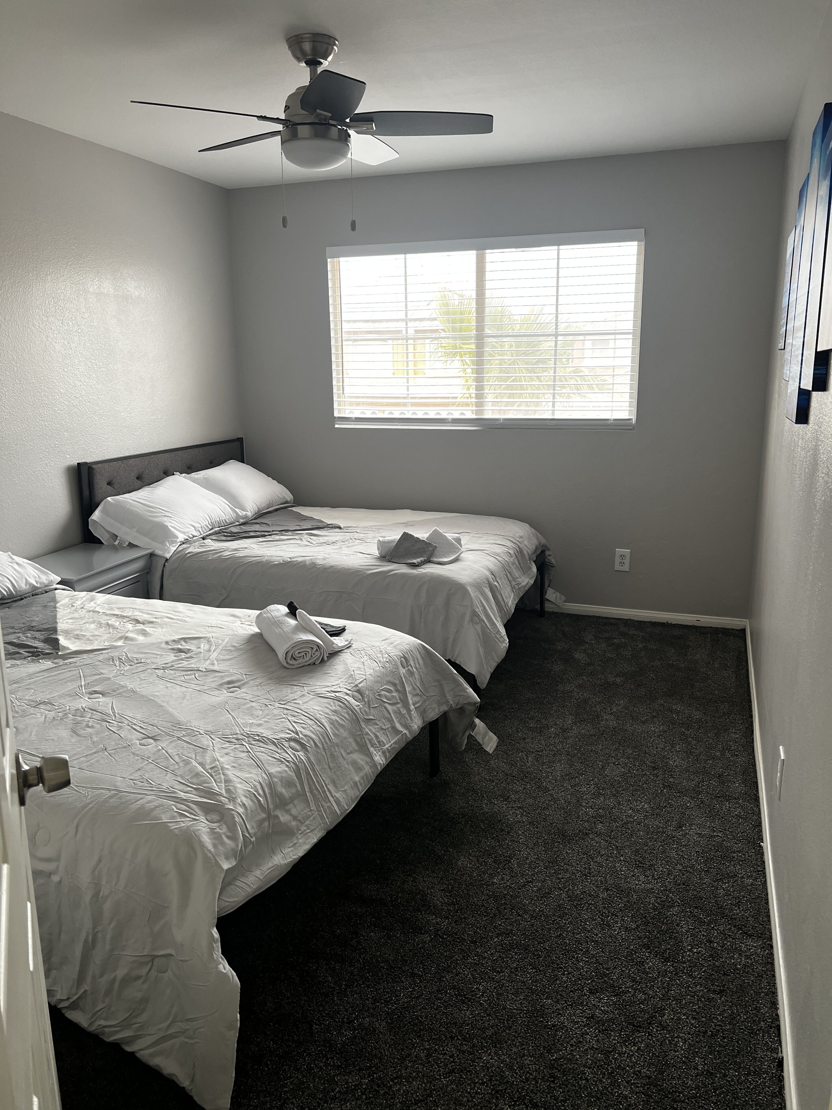 Een slaapkamer met twee bedden, een plafondventilator en een groot raam.