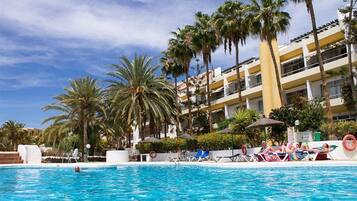 Un área de piscina con sillones de descanso y palmeras.