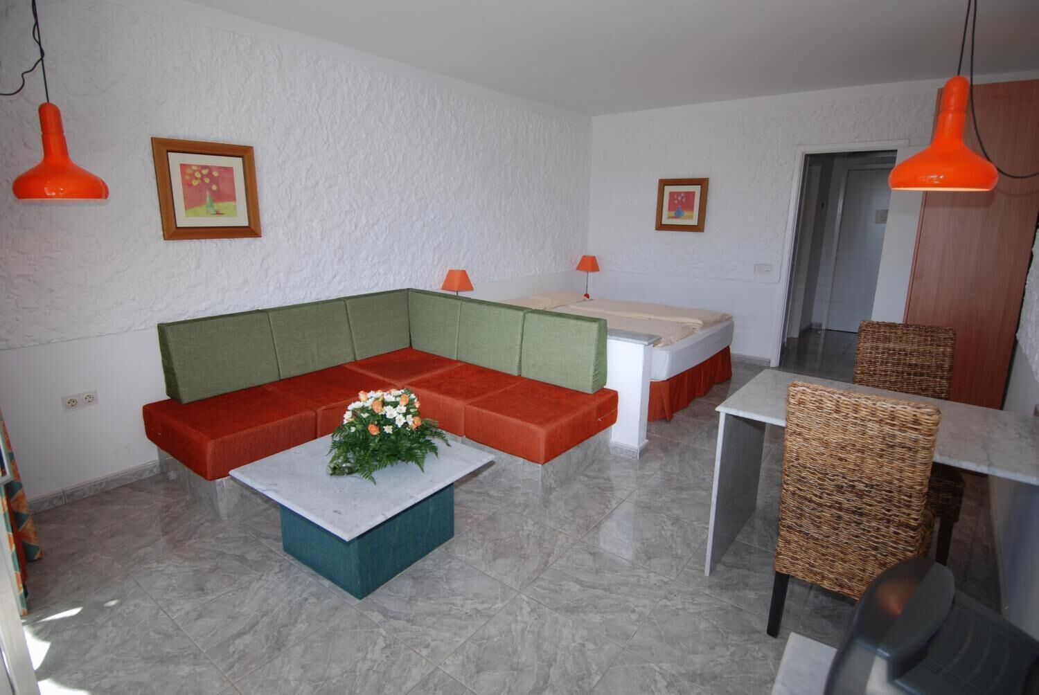 Ein modernes Wohnzimmer mit einem Ecksofa, einem Couchtisch, einem Esstisch mit Korbstühlen und zwei Pendelleuchten.