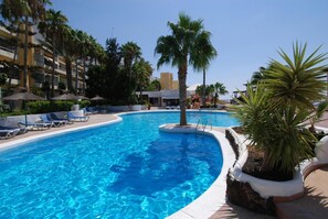 A swimming pool with lounge chairs and palm trees, surrounded by hotel buildings.