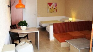 Une pièce de taille modeste comprenant un lit, un canapé, une table à manger avec des chaises et une petite table avec une lampe.
