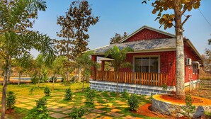 Una casa de ladrillo rojo con un porche de madera, rodeada de un jardín con un sendero a cuadros y diversas plantas.