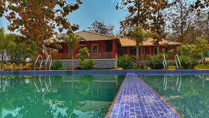 Una piscina con borde de azulejos azules, rodeada de árboles y un edificio con fachada de ladrillo rojo.