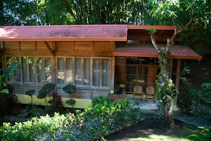 Surrounded by lush greenery, this house features large windows and a cozy porch with a chair.