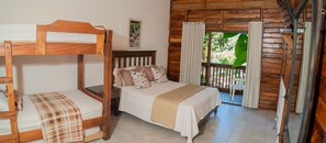 Cozy bedroom with a wooden bunk bed and single bed, a wooden table, and a window with curtains.