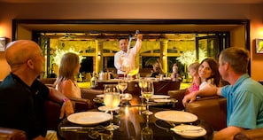 A restaurant with a bar area where a bartender is serving drinks. There are tables with diners and a view of the outdoors through large windows. - Villa Del Palmar Loreto - 3 Bedroom Villa - Sleeps 10 - CHRISTMAS WEEK SPECIAL
(Loreto)