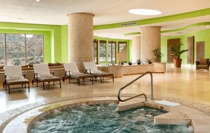 A spa area with a hot tub, lounge chairs, and large windows offering a mountain view.