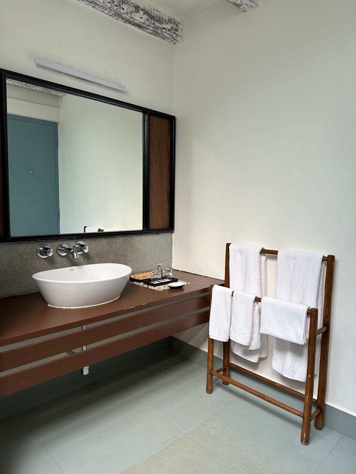 Une salle de bain moderne avec un grand lavabo blanc, un miroir et un porte-serviettes en bois.