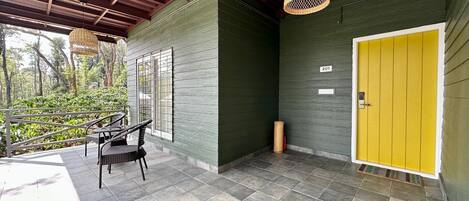 A covered outdoor area with a green wall, a yellow door, and a wicker hanging light fixture.