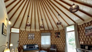 Una habitación amplia con una cama grande, una mesa de comedor y un sofá. Hay lámparas colgantes y una ventana que proporciona luz natural.