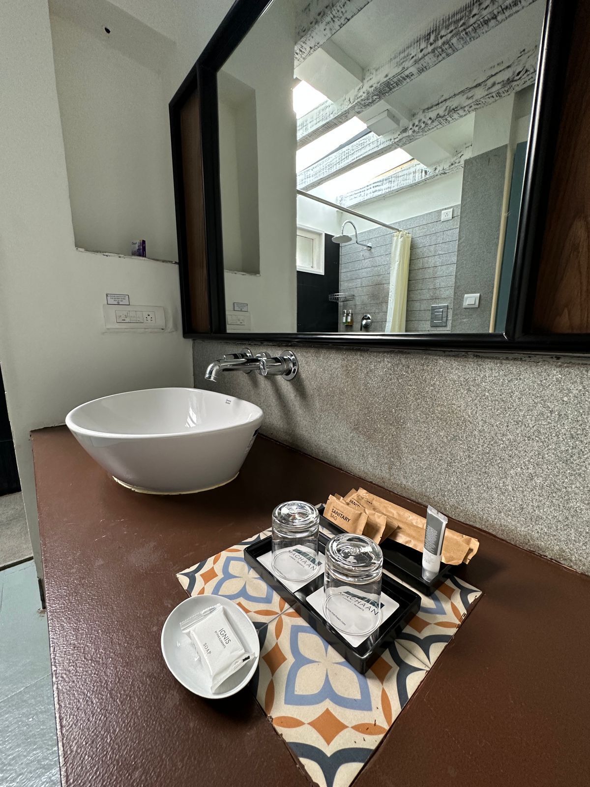 A bathroom with a large white sink, a mirror, and a tray with toiletries.