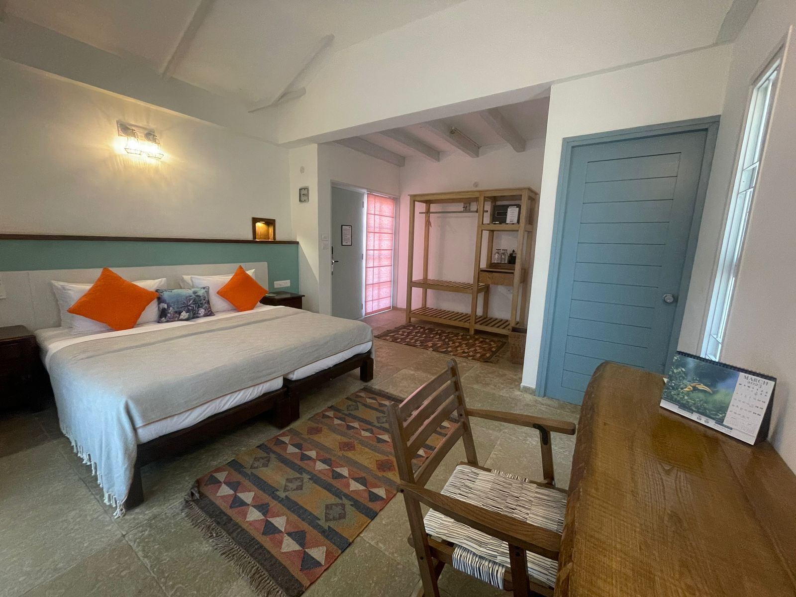Une chambre d’hôtel avec un lit, un bureau, une chaise, une étagère en bois et un calendrier accroché au mur.