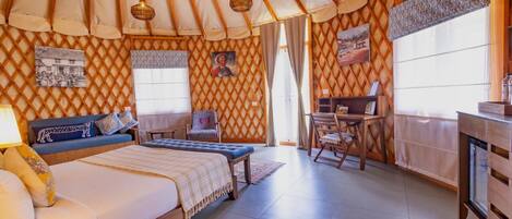 A room with a bed, a desk, and a chair. There is a window with curtains, a wall with a lattice pattern, and a hanging light fixture.