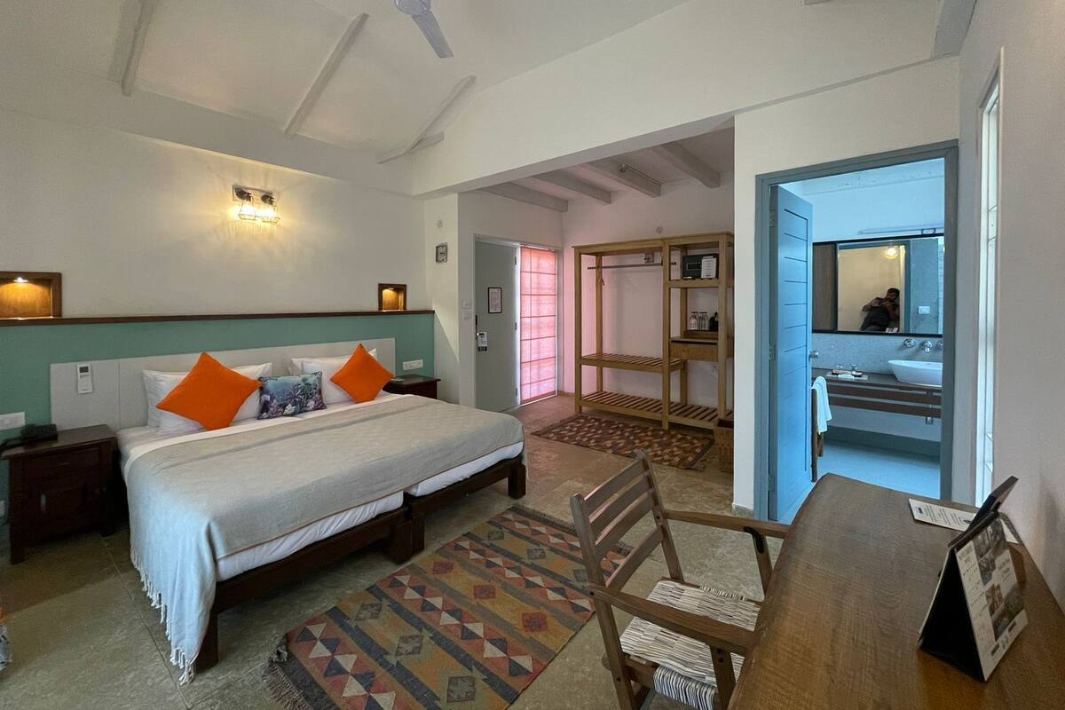 Habitación de hotel con cama, escritorio, silla, armario, espejo y baño.