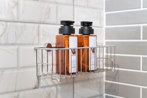 A bathroom with white marble tiles and a metal shelf holding two bottles of Hotel WOW shampoo. - Hotel Wizpark Ratchada (Bangkok)