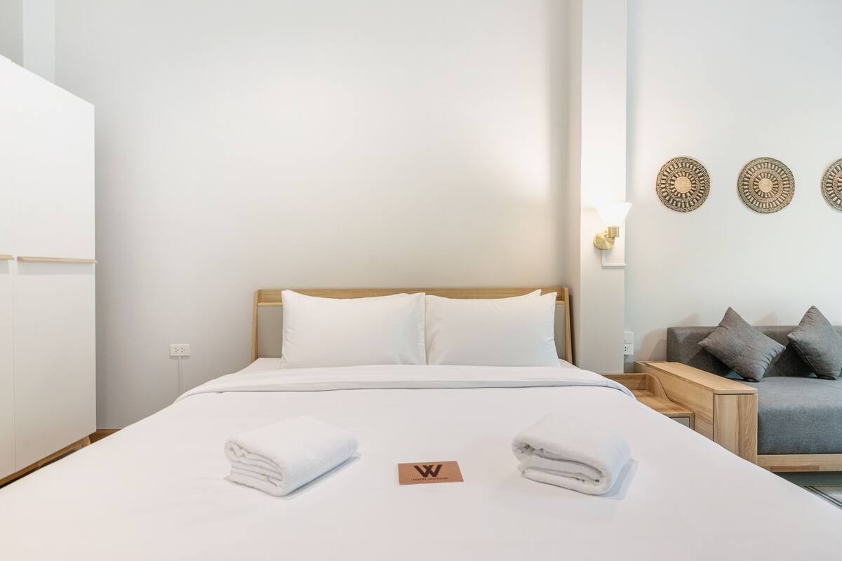 A hotel room with a large bed, a wooden headboard, white bedding, a grey sofa, and decorative wall plates.