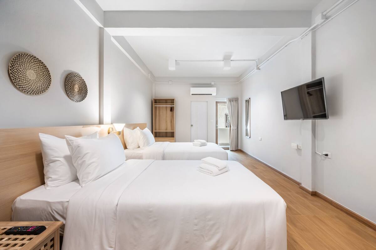 A modern hotel room with two beds, a wooden headboard, a TV mounted on the wall, and a walk-in closet.