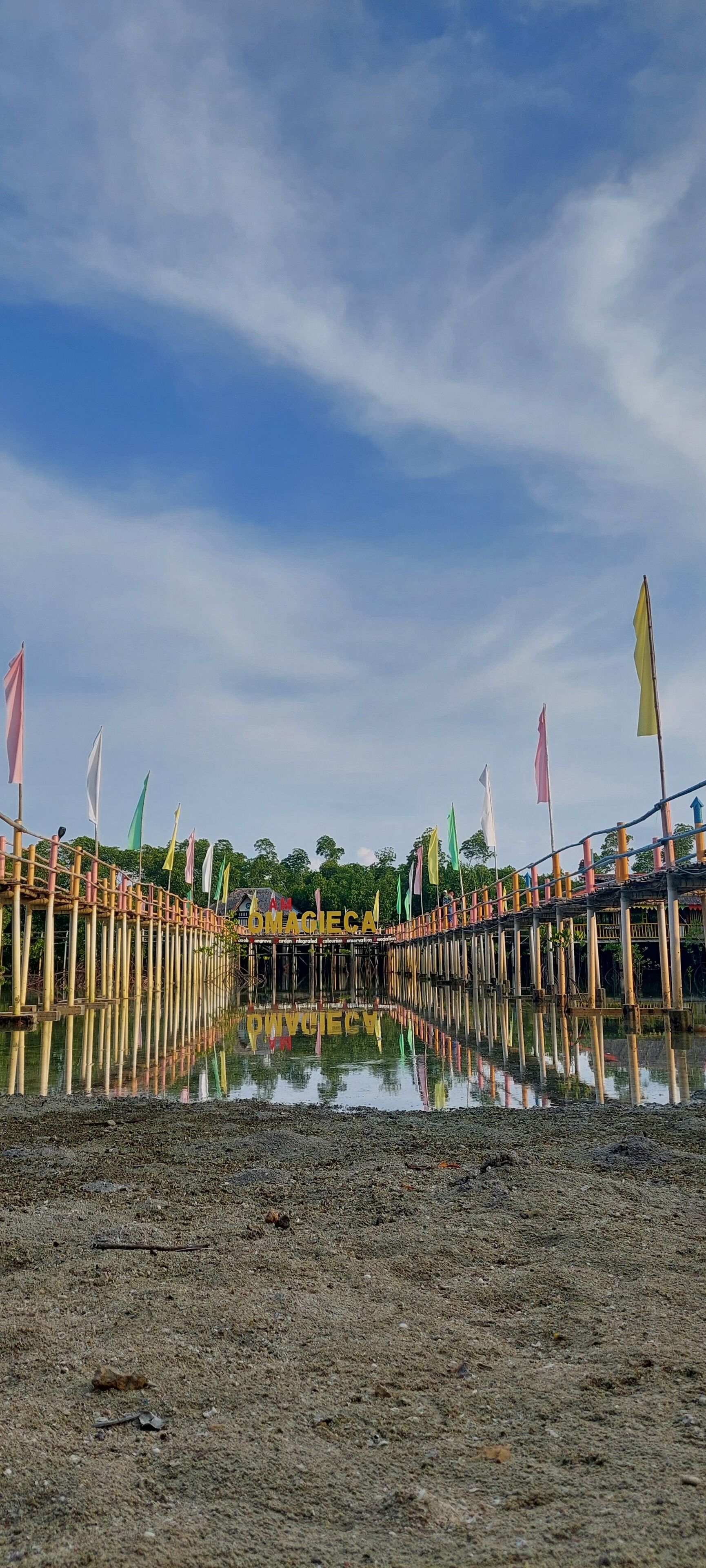 A wooden bridge with colorful flags extending over a calm body of water.