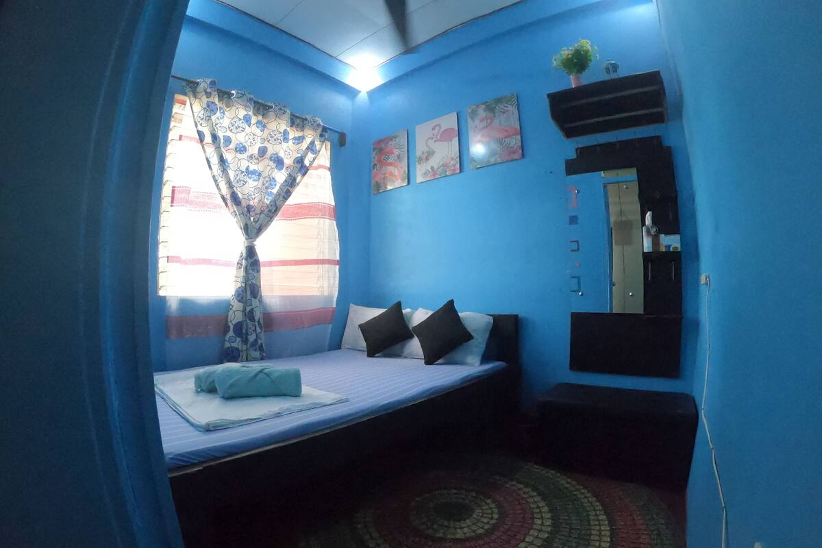 A room with a bed, a window with curtains, a mirror, and a wall with artwork.