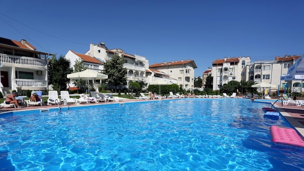 Una piscina con lettini e ombrelloni, circondata da edifici a più piani con balconi.