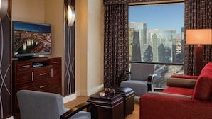 Une chambre d’hôtel avec vue sur la ville, une télévision, un bureau et deux coins salon.