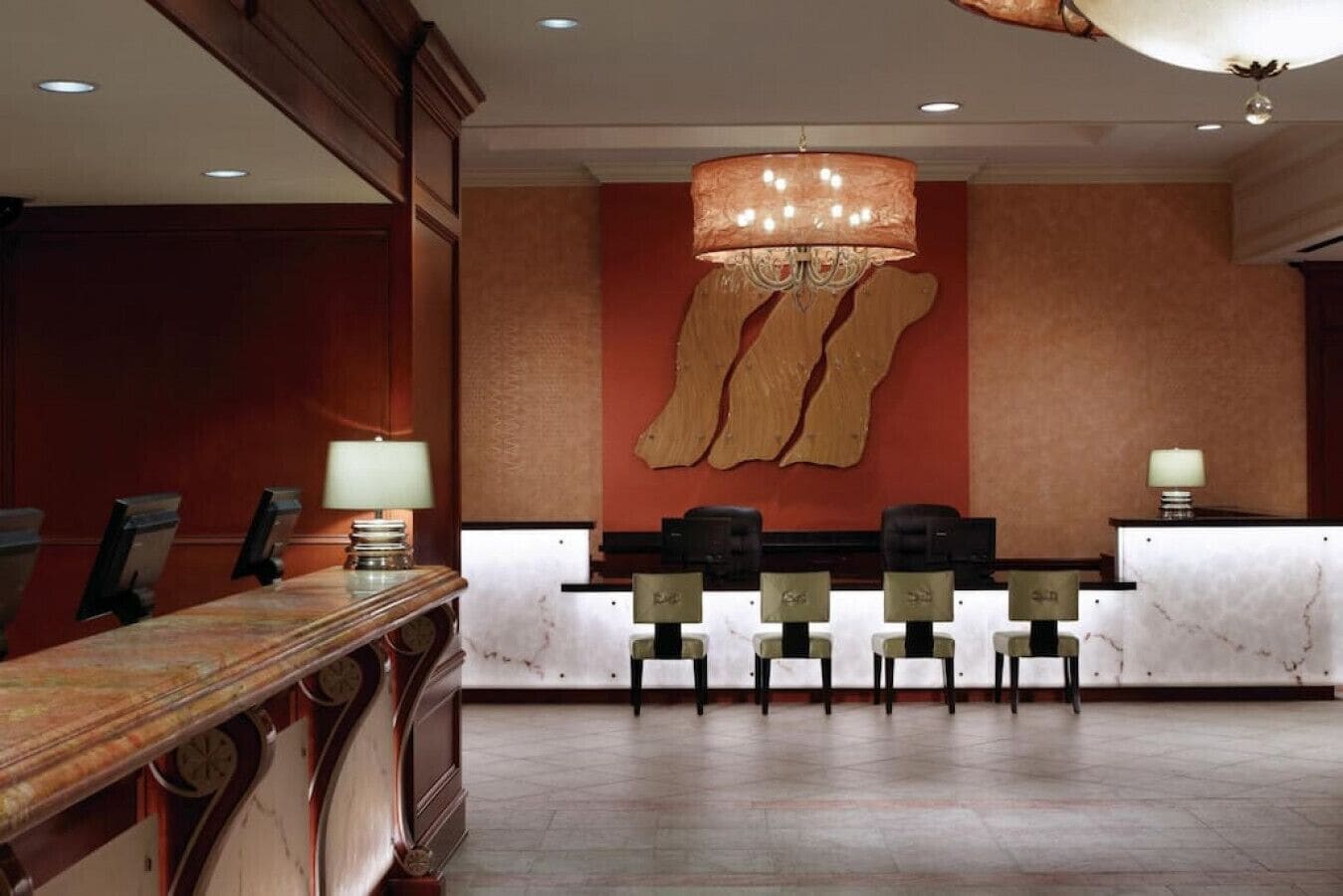 A reception area with a marble counter, several chairs, a chandelier, and a large abstract wall piece.