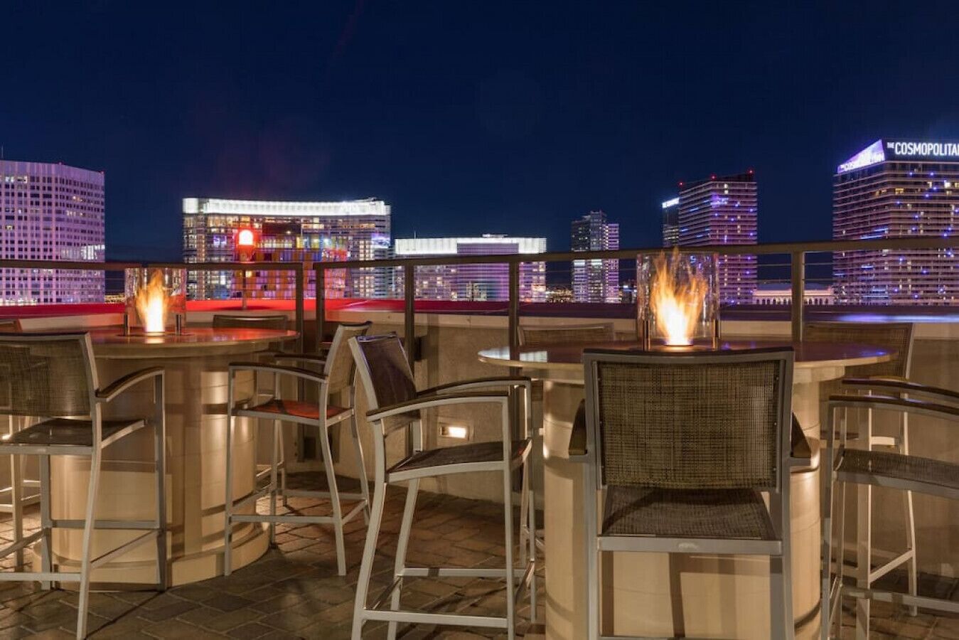 Eine Dachterrasse mit Sitzgelegenheiten im Freien und Blick auf den nächtlichen Stadtpanoram.