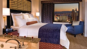 Une chambre d’hôtel comprenant un lit, un bureau avec une lampe, une chaise, une grande fenêtre donnant sur la ville, ainsi qu’une salle de bain avec un lavabo et un miroir.