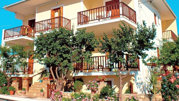 Un edificio de varios pisos con balcones, plantas en macetas y un cielo azul despejado.