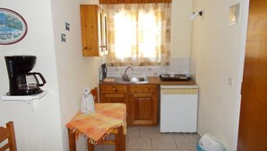 Cocina compacta con armarios de madera, cafetera, hervidor y una pequeña mesa de comedor con mantel.