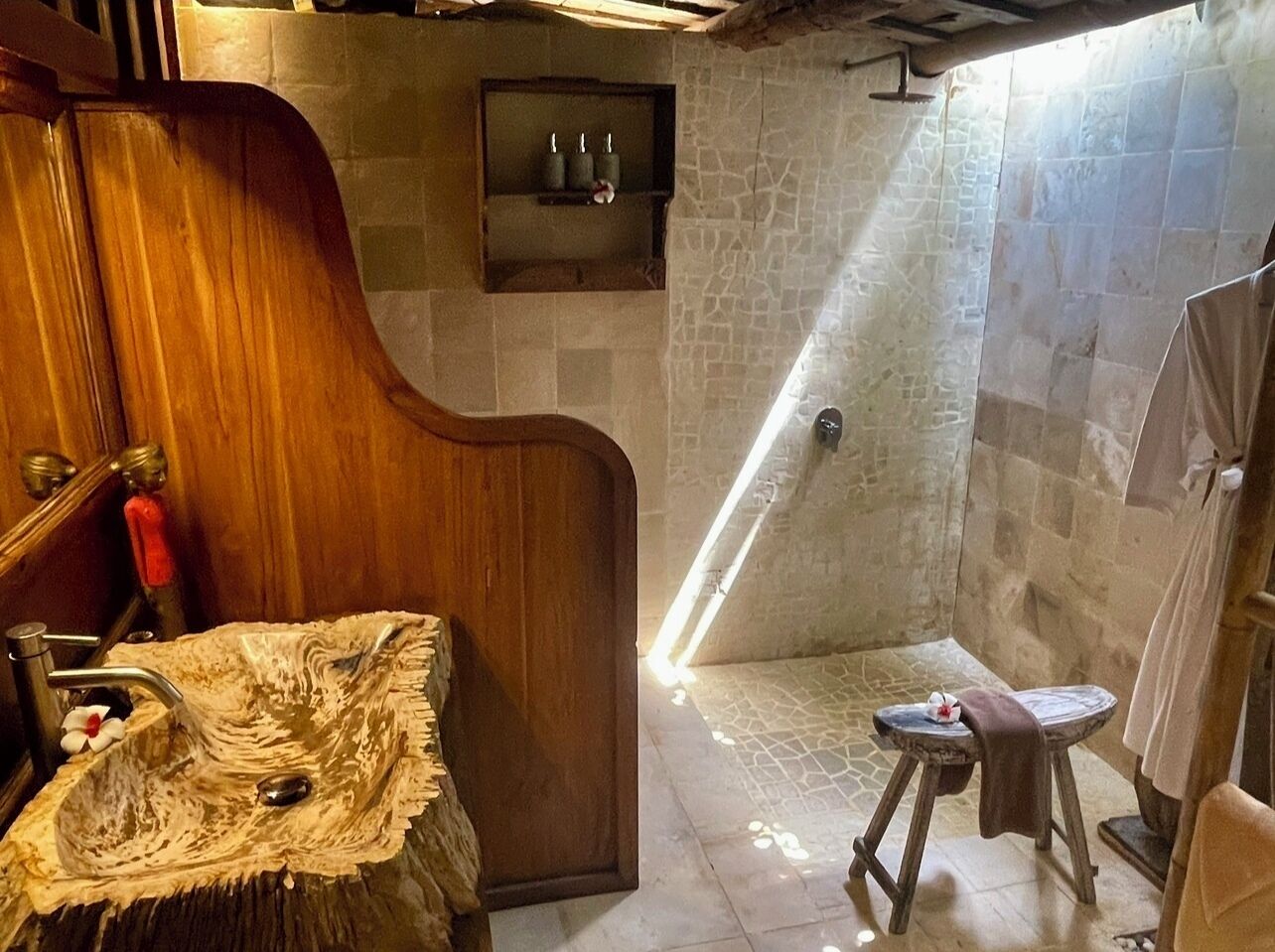 A bathroom with a wooden vanity, a stone shower, and a small stool with a towel.