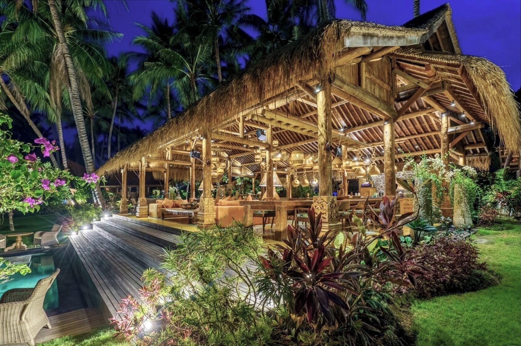 A thatched-roof structure with outdoor seating and a pool, surrounded by tropical vegetation.