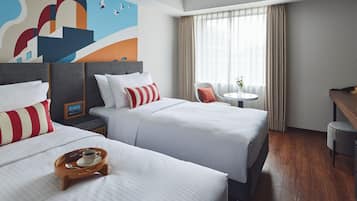A hotel room with two beds, a small table with a cup and saucer, a chair, and a painting on the wall.