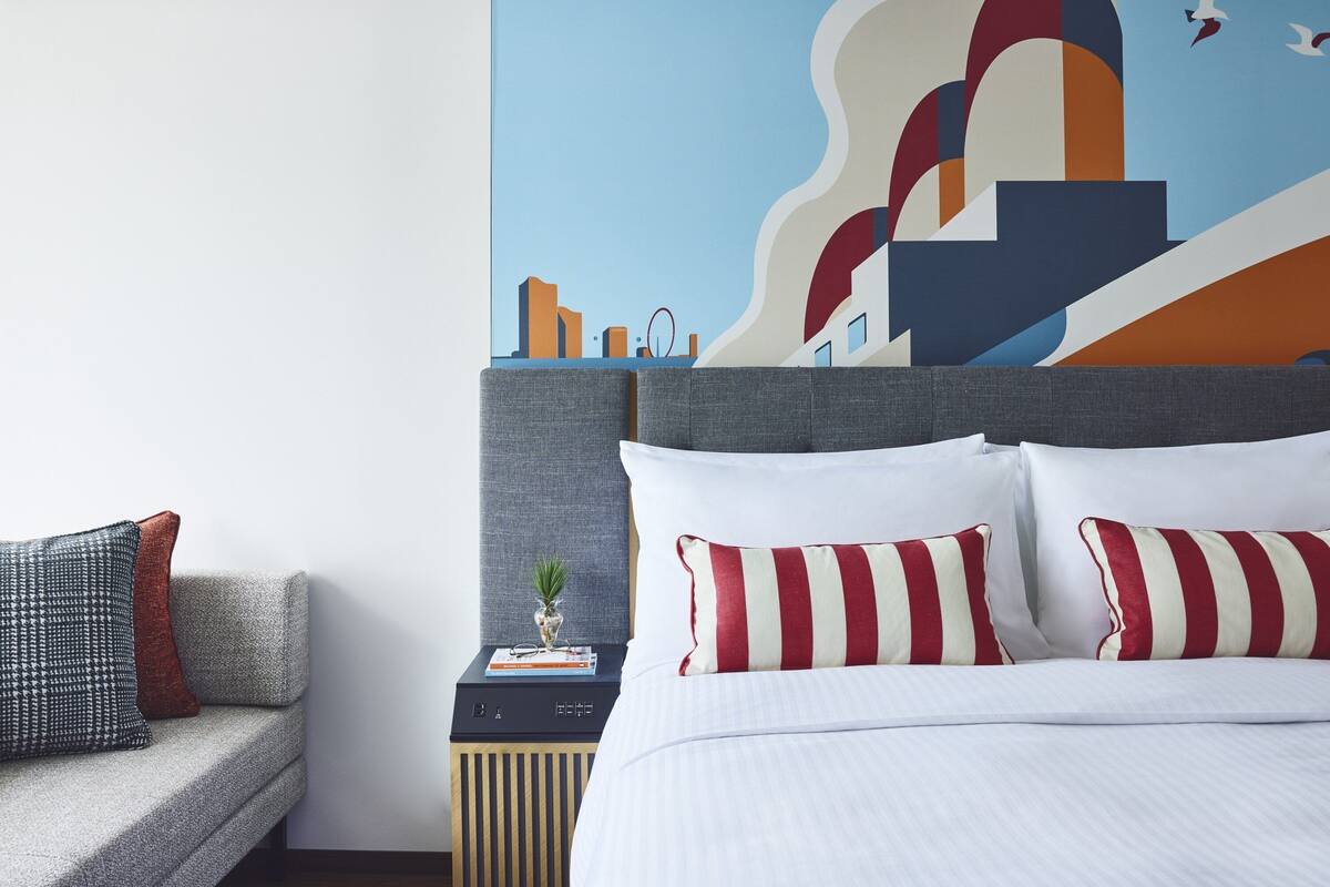 A hotel room with a bed, a nightstand, a sofa, and a wall mural.