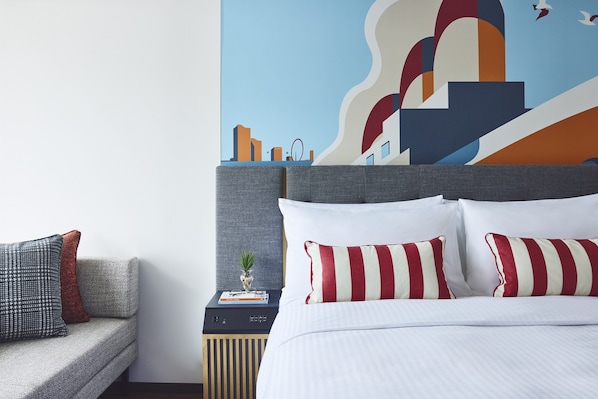 Una habitación de hotel con cama, mesita de noche, sofá y un mural en la pared.