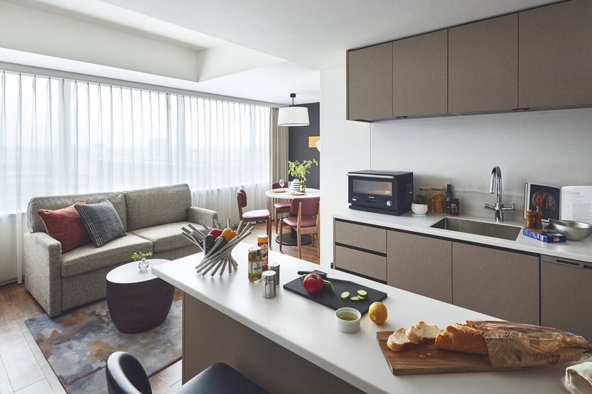 A modern kitchen with a central island, a dining area with a sofa and chairs, and a large window with sheer curtains.