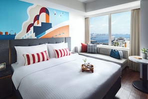 Una habitación de hotel moderna con una cama grande, vistas al puerto y un mural urbano en la pared.