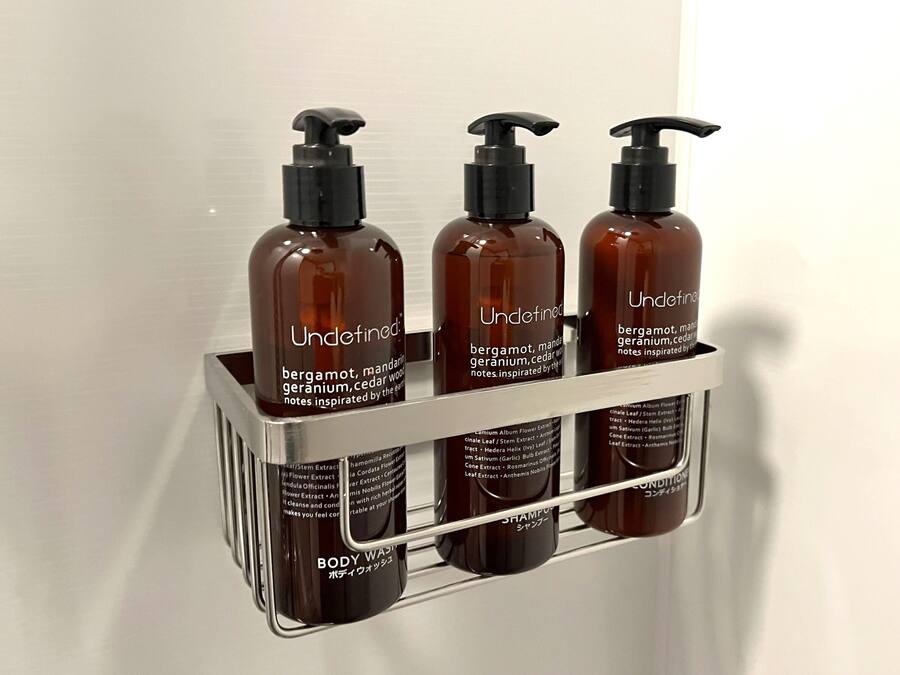 Uno scaffale in bagno con tre flaconi di bagnoschiuma e una bottiglia di shampoo.