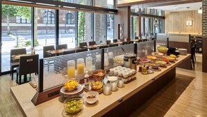 Ein Buffet mit verschiedenen Speisen und Getränken, eine Sitzgelegenheit mit Tischen und Stühlen sowie große Fenster mit Blick auf die Straße.